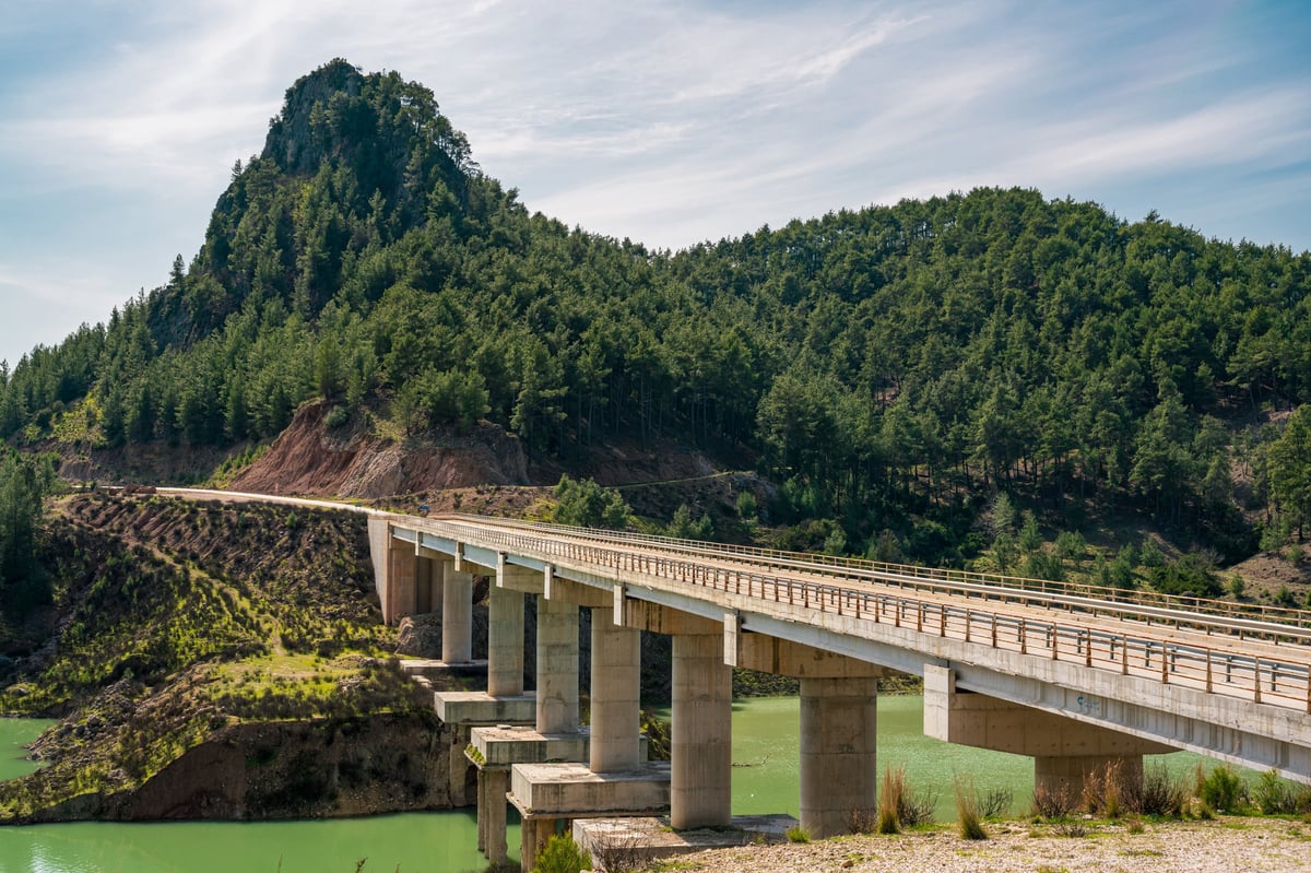 Bridge spanning an emerald reservoir surrounded by forested mountains
